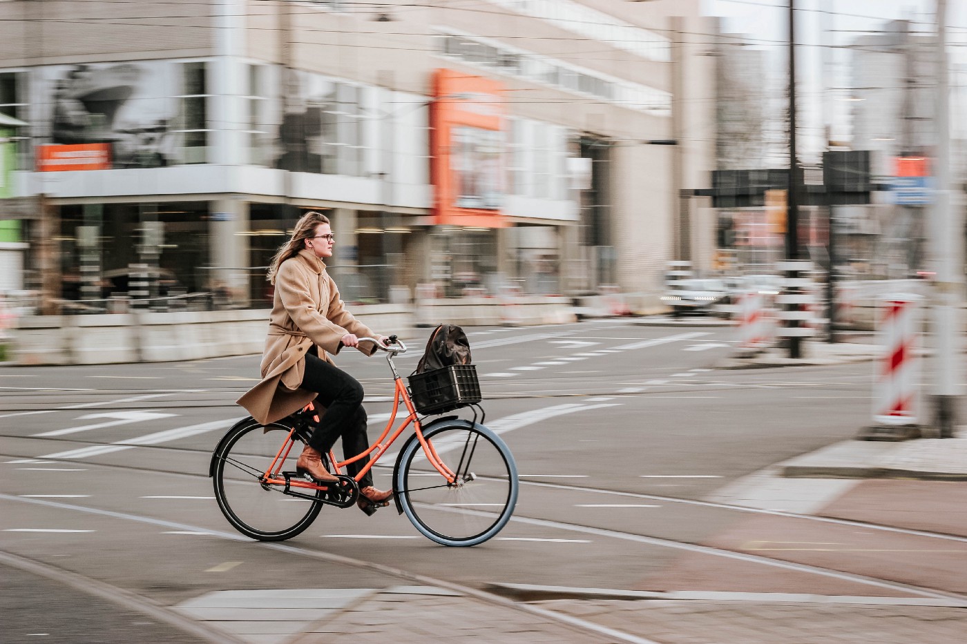 A woman rides an orange bike from left to right. Physical activity can reduce the risk of stroke.