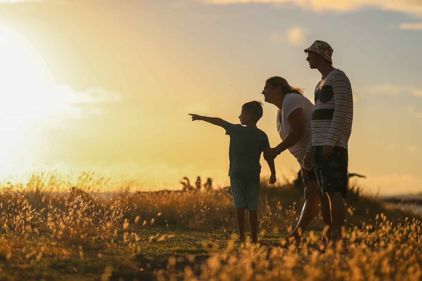 As the sun sets, an older couple looks on as a young boy points to the left of the image.