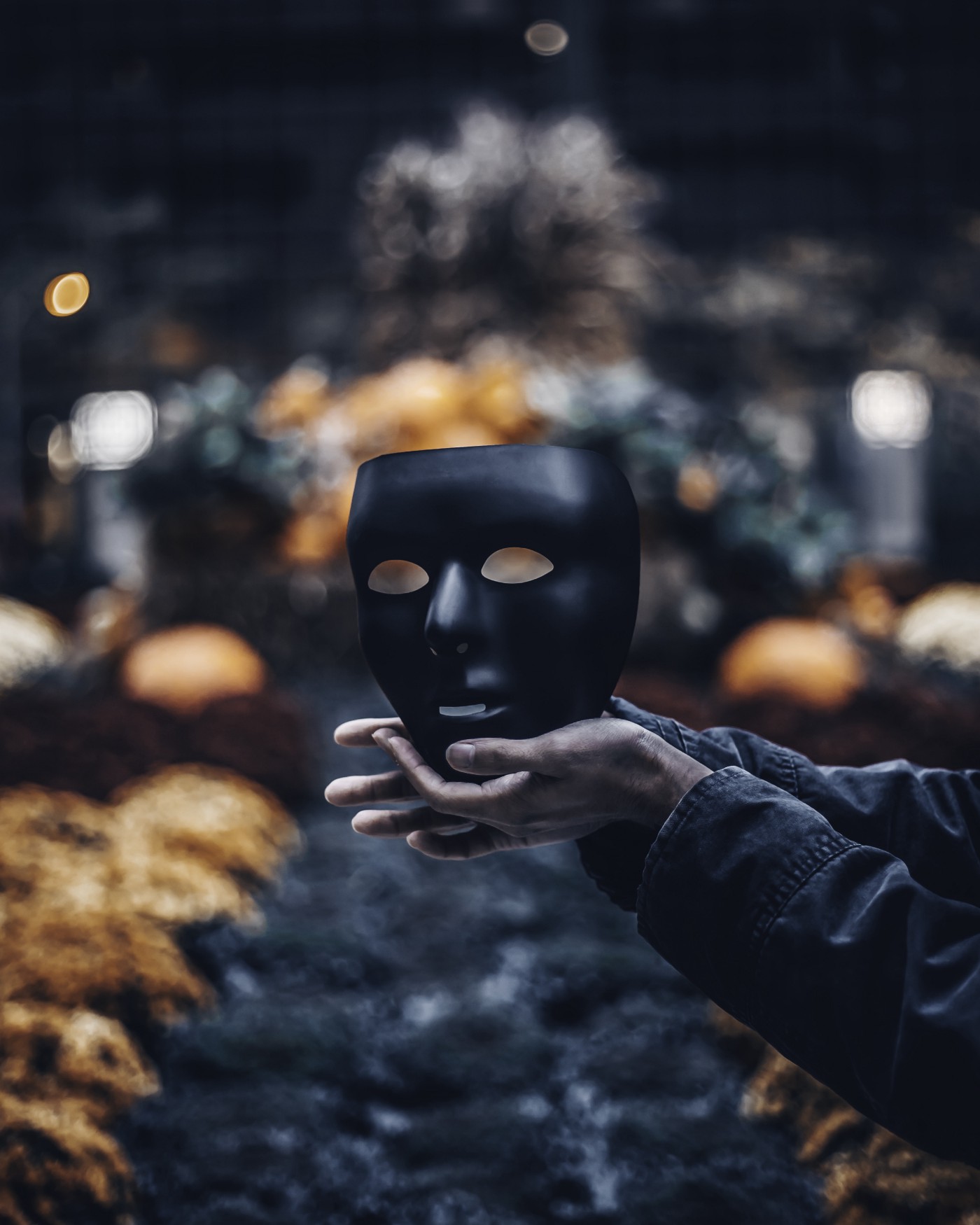Arms extend from the image’s lower right to hold a black stage mask vertically.