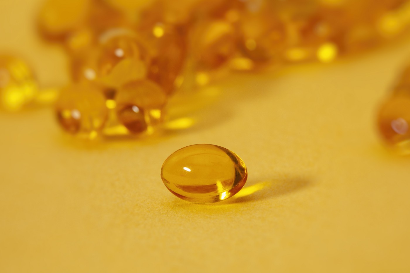 Several yellow, oblong vitamin E capsules, set against a yellow backgroun.