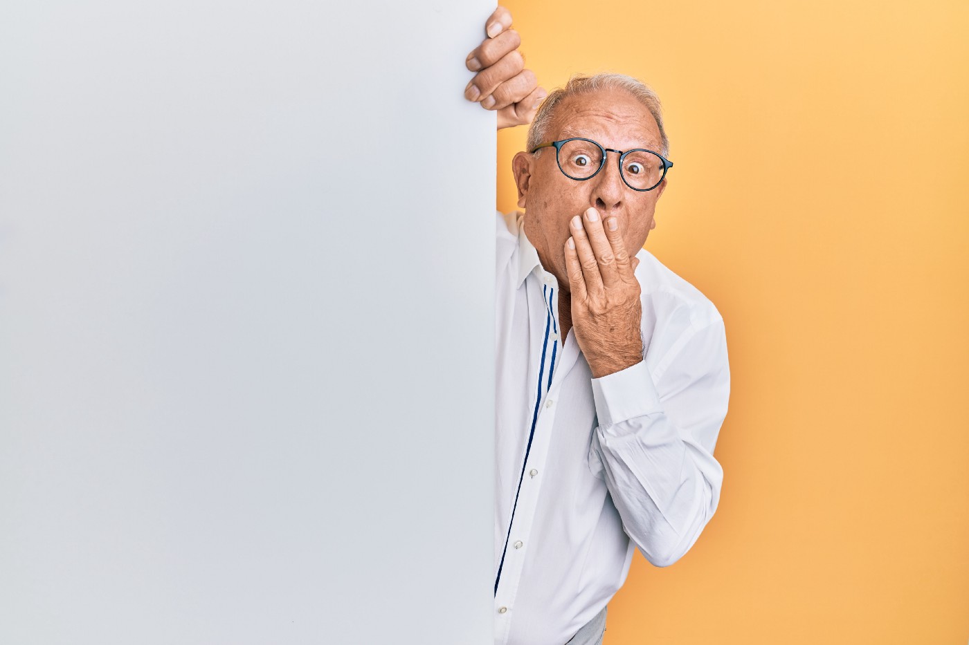 Older white male looks surprised, his had lifted to cover his mouth and his eyes open wide.