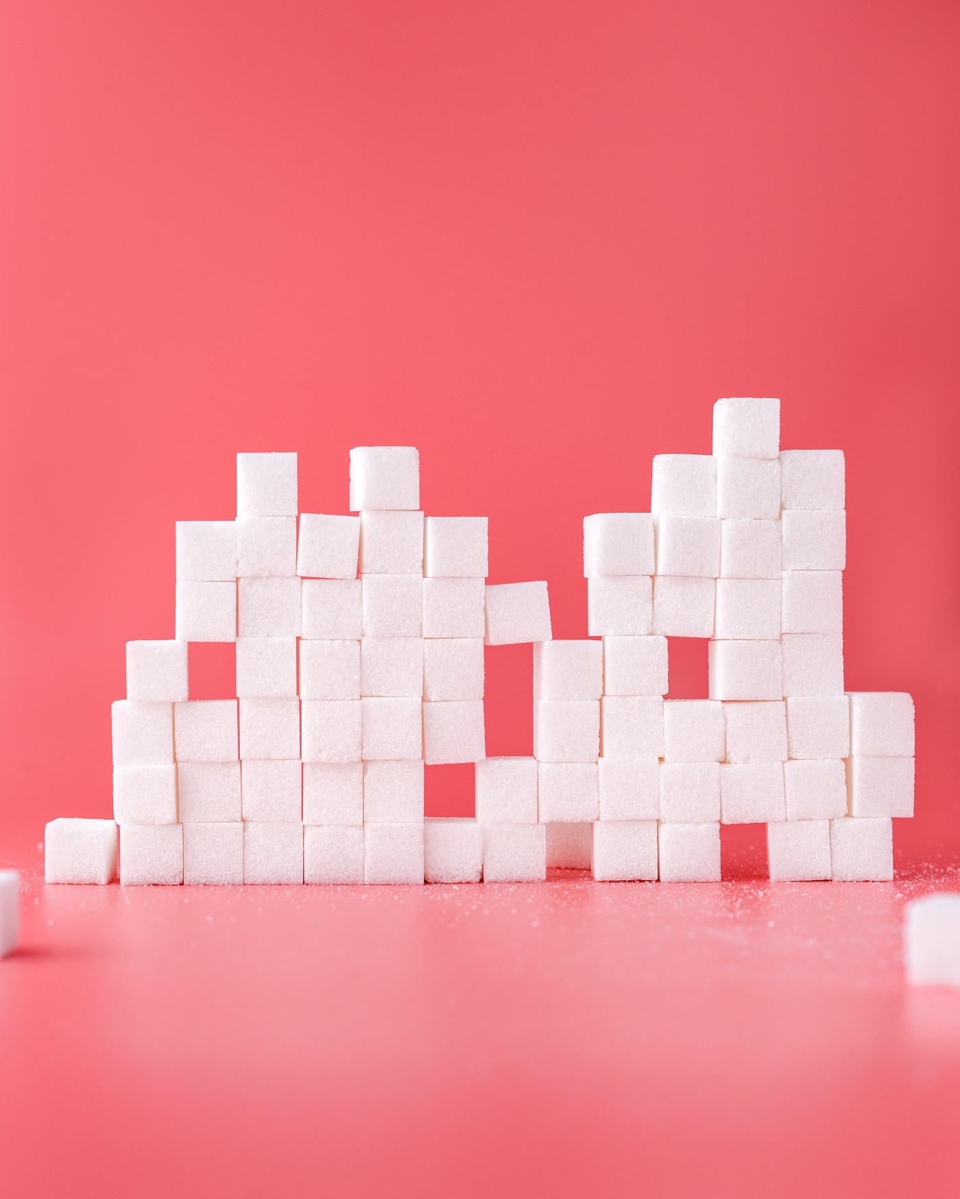A stack of sugar cubes, numbering about 15 from left to right and seven cubes high. There are missing cubes in several locations. Pinkish background.