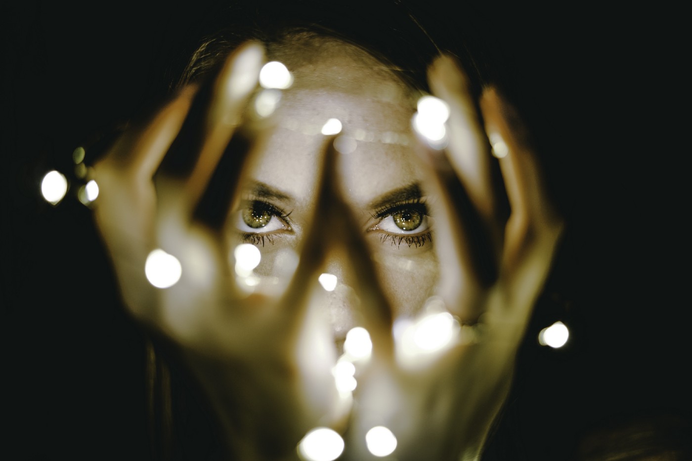 A woman gazes intensely at us, her blue eyes seen through fingers that are holding a strand of light.