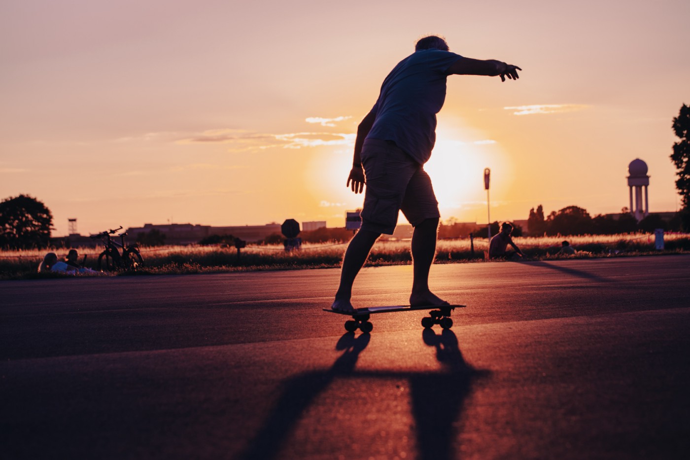 An overweight man rides a skateboard as the sun sets in the distance.