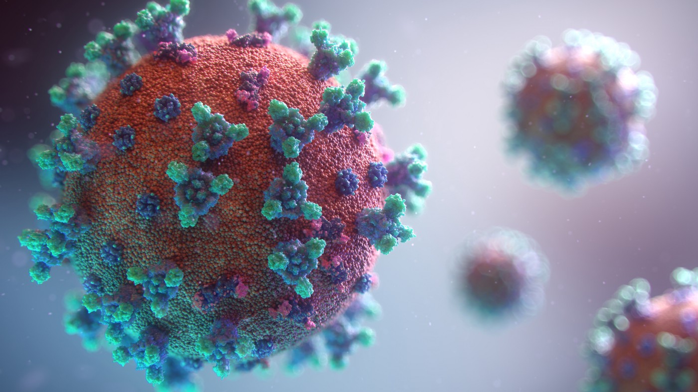 COVID-19 particles, drawn with red bodies and green and blue antennae-like appendages. There is one dominant COVID-19 virus occupying most of the left foreground, with three blurred and smaller particles in the background on the right.