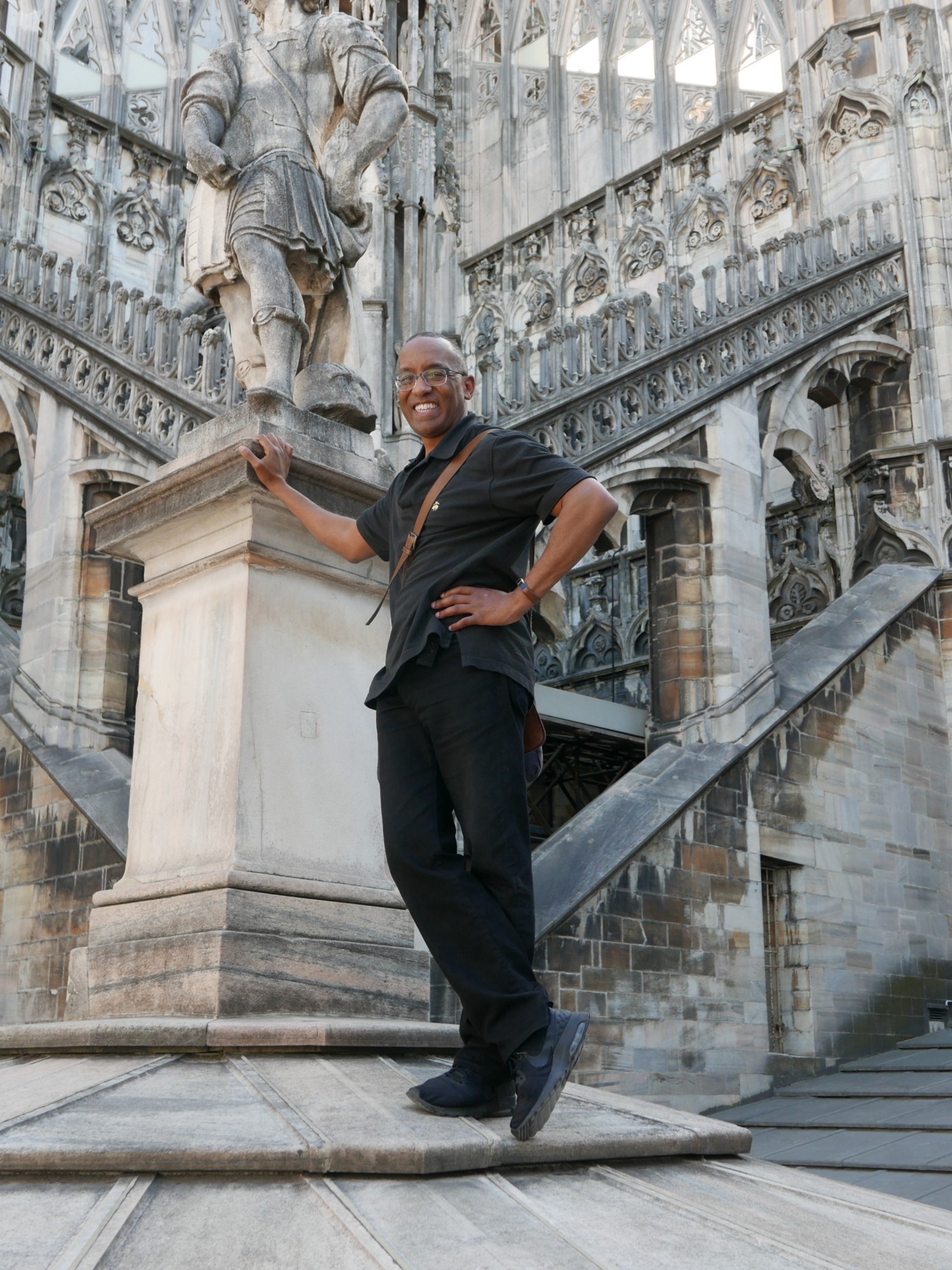 A smiling Dr. Michael Hunter, dressed in a black shirt and black pants, stands on the stairs of the Cathedral in Milan.