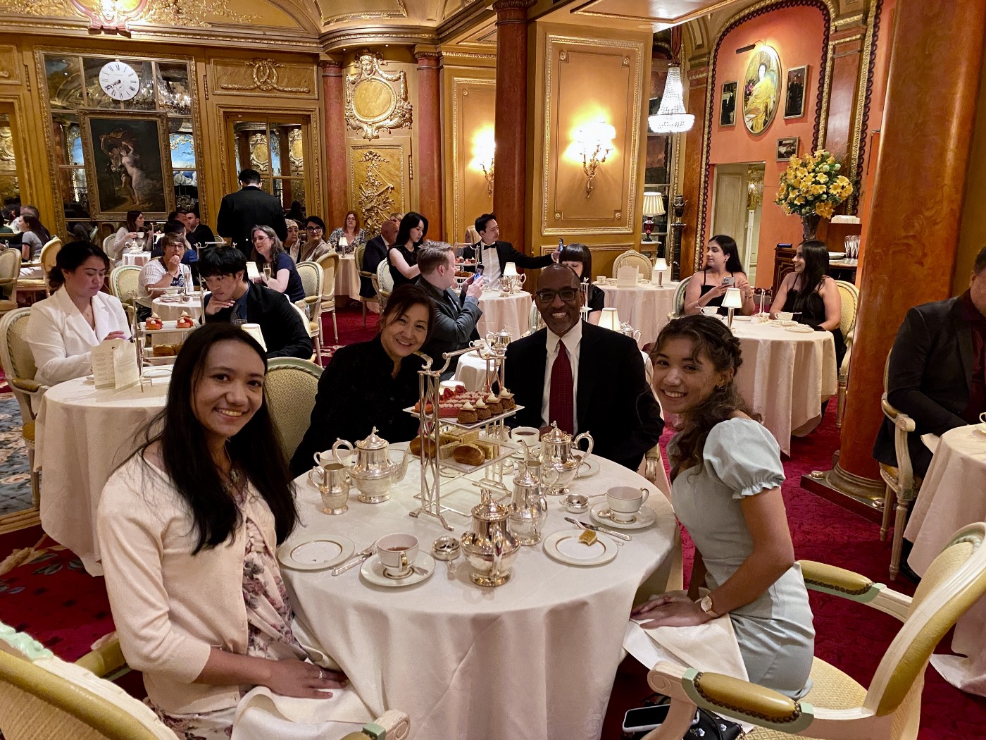 The author, his wife, and two of their children sit at a table with a white tablecloth for afternoon tea. The fete is at London’s Ritz Hotel.