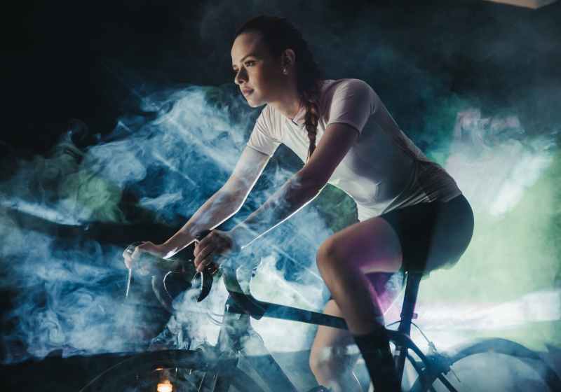 focused sportswoman riding bike in artificial smoke