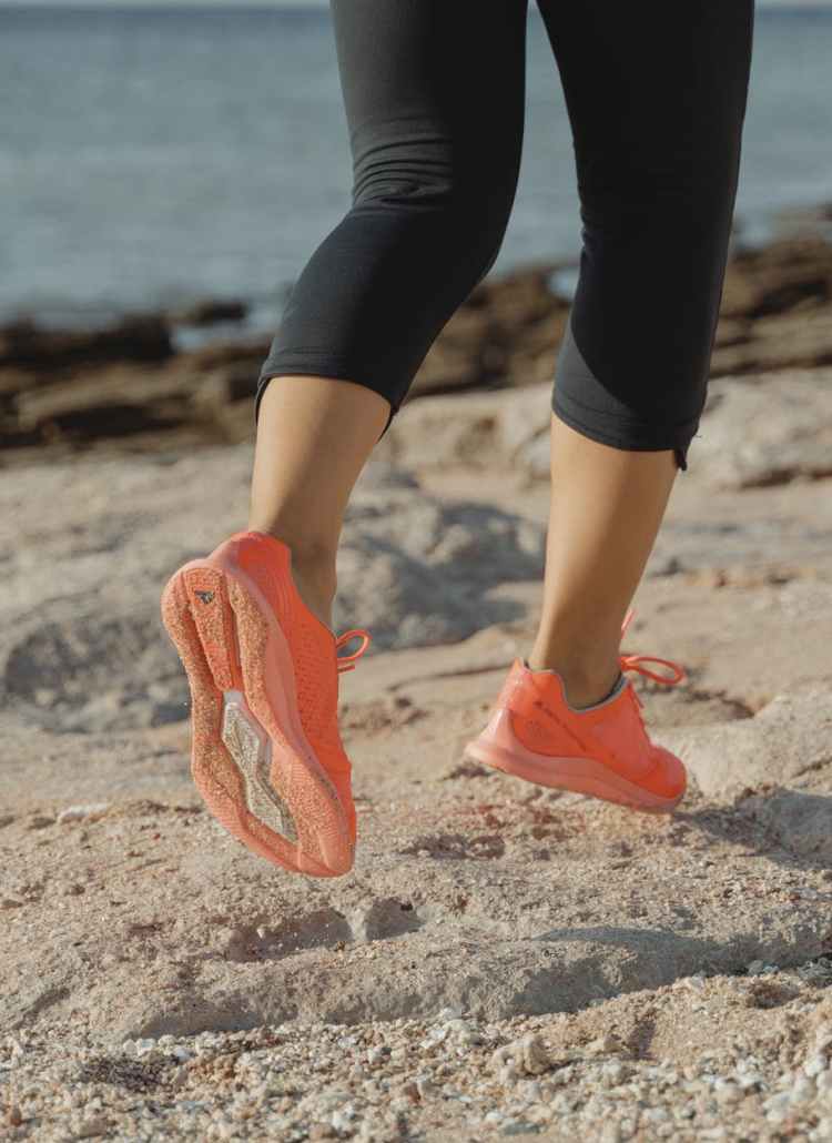 woman in black leggings and orange sneakers standing on brown sand near body of water during