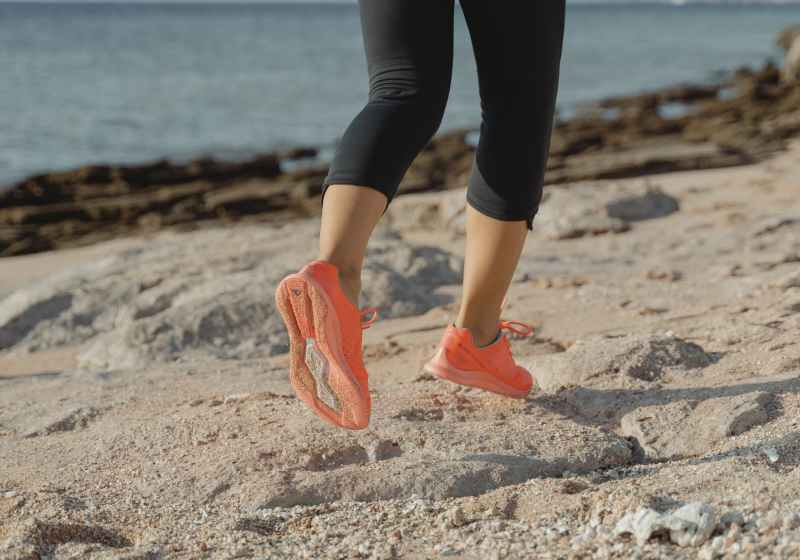 woman in black leggings and orange sneakers standing on brown sand near body of water during