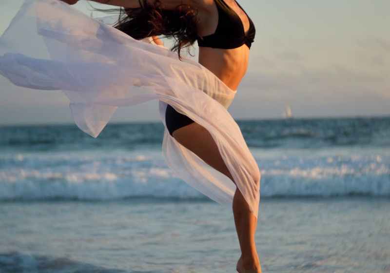 skinny dancer jumping over sandy shore of ocean