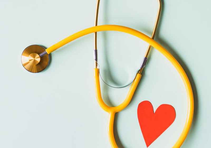 medical stethoscope with red paper heart on white surface