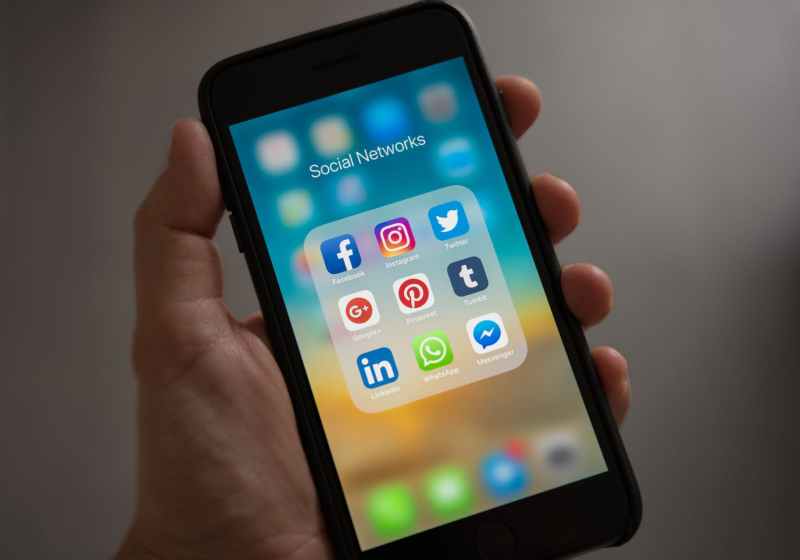 person holding iphone showing social networks folder