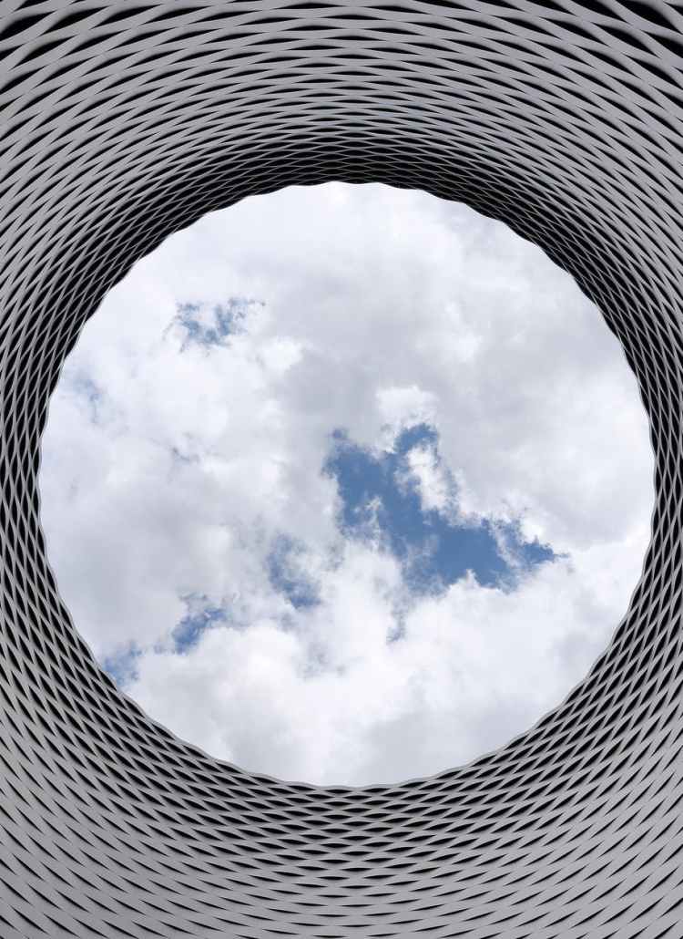 low angle photography of grey and black tunnel overlooking white cloudy and blue sky