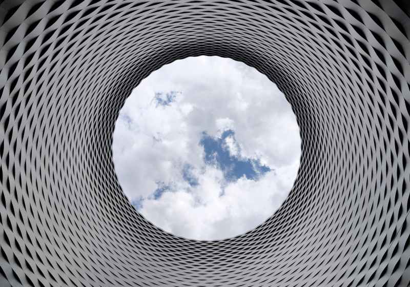low angle photography of grey and black tunnel overlooking white cloudy and blue sky