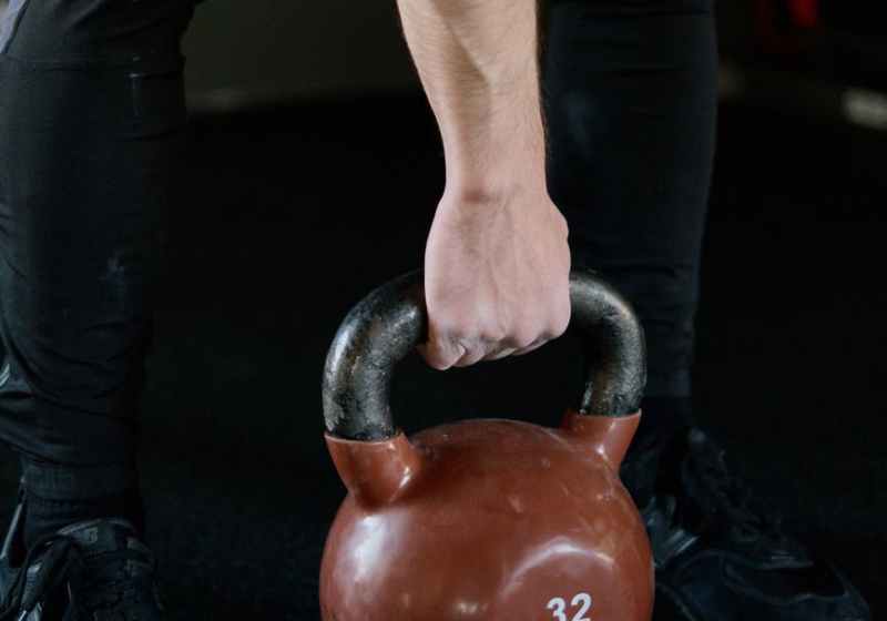 person in black pants holding red kettlebell