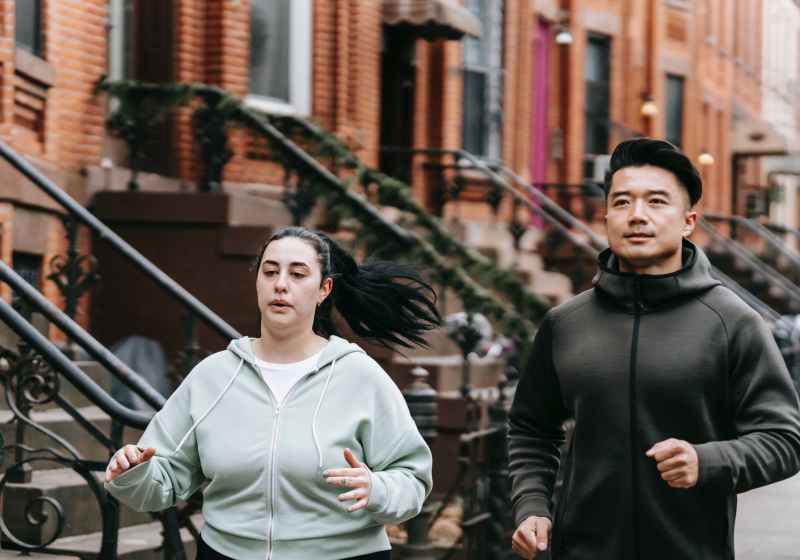 active young diverse man and woman running on street near residential buildings