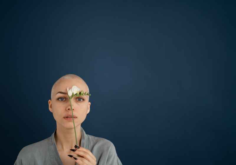 woman with blossoming freesia and shaved head on blue background
