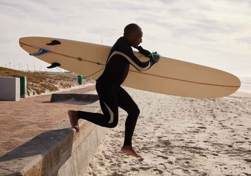 black surfer running to ocean with surfboard in daytime