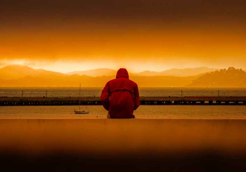 person wearing red hoodie sitting in front of body of water