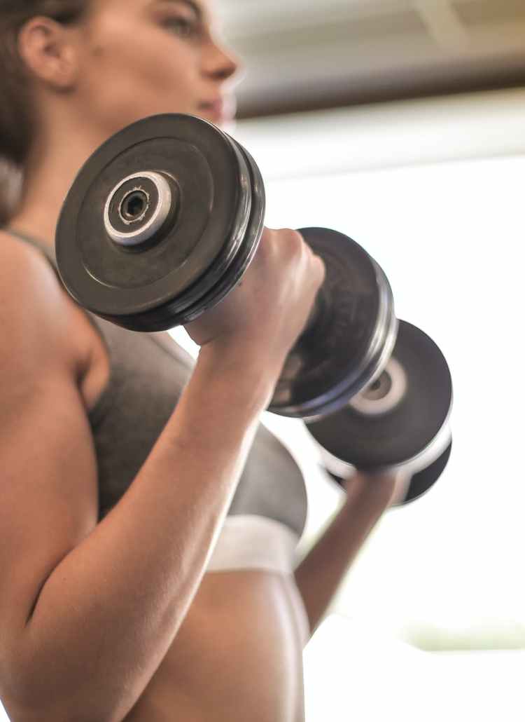 woman in gray sports bra holding black dumbbell