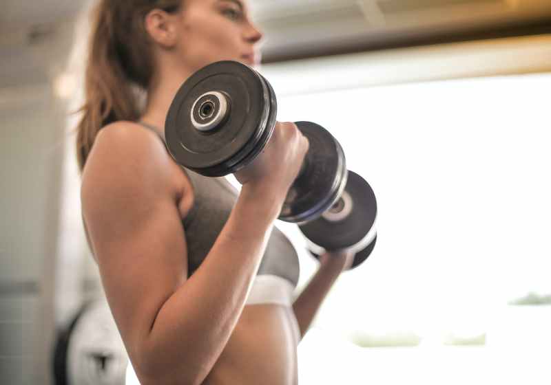 woman in gray sports bra holding black dumbbell