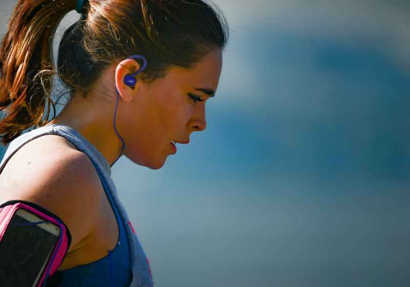 woman wearing smartphone armband and blue earphones
