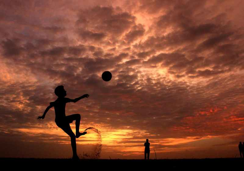 silhouette of a boy playing ball during sunset