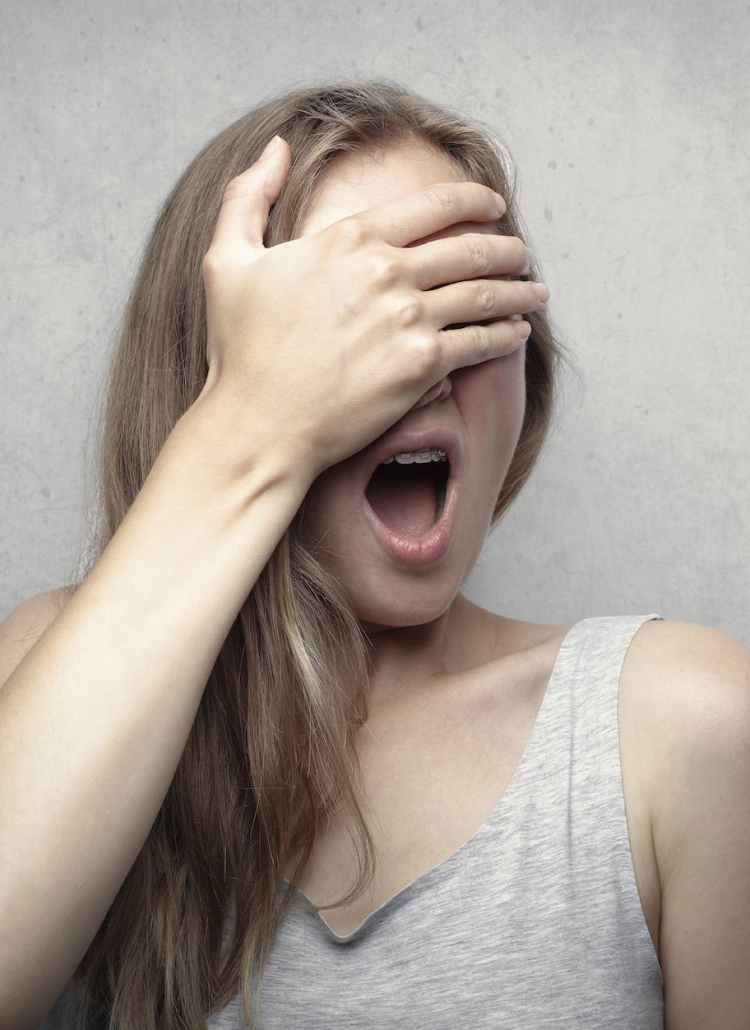 woman in gray tank top covering her face with her hand