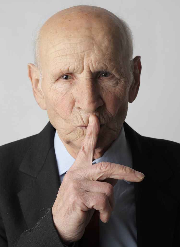 elderly gentleman making silence gesture in studio