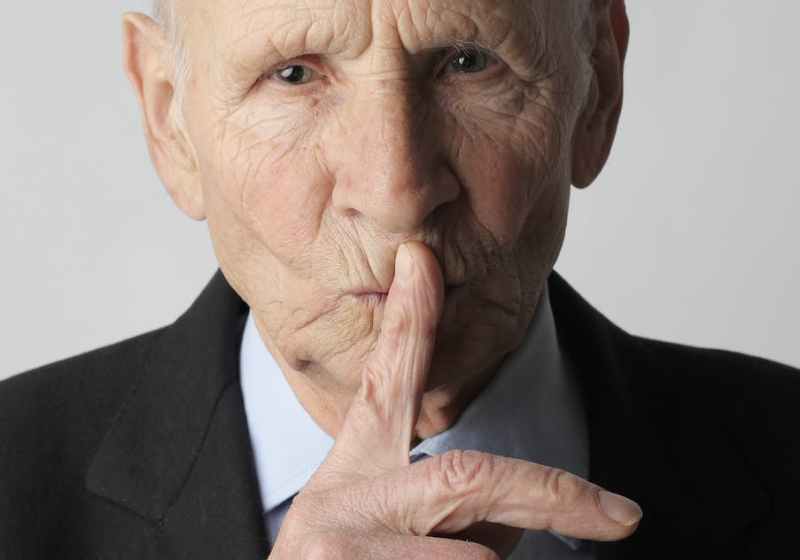 elderly gentleman making silence gesture in studio