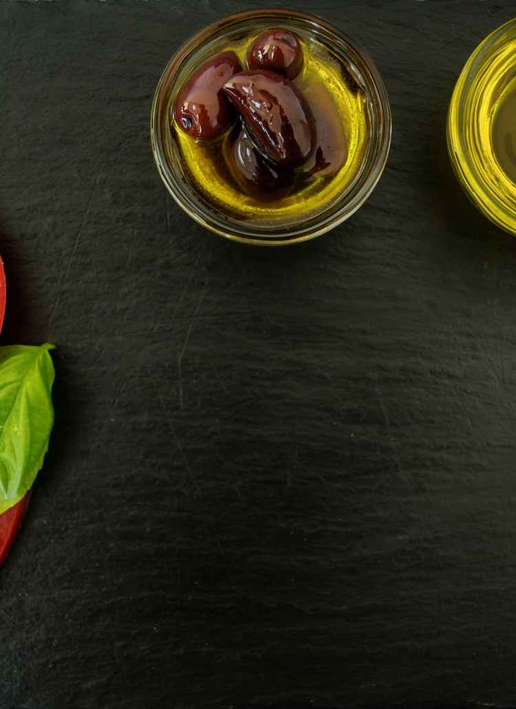 sliced tomatoes with basil leaves and two cooking oils on black wooden surface