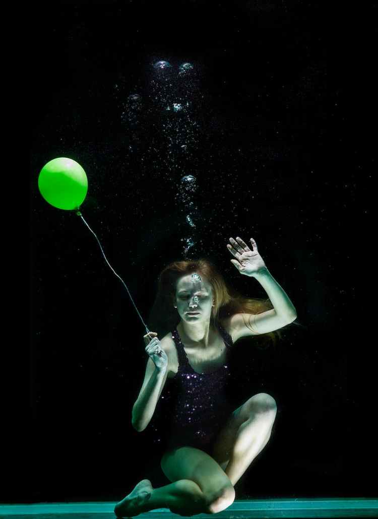 underwater photography of woman holding green balloon