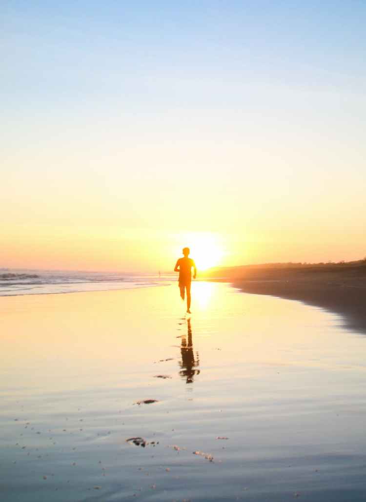 silhouette of boy running in body of water during sunset