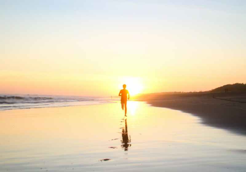 silhouette of boy running in body of water during sunset