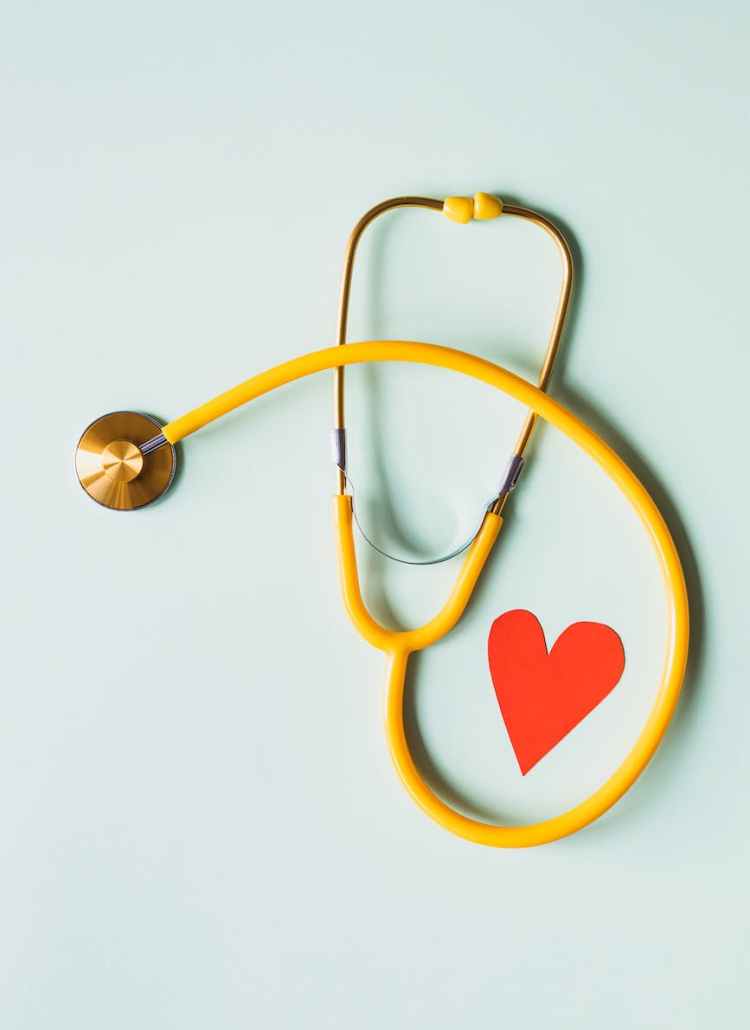 medical stethoscope with red paper heart on white surface