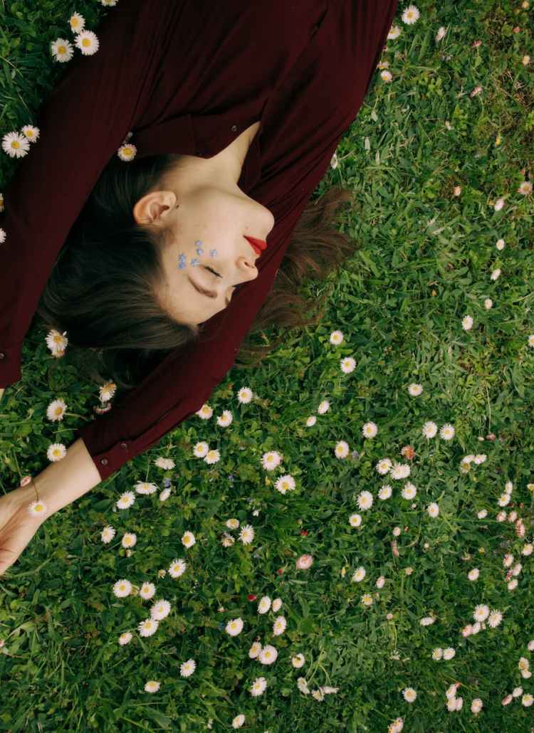 woman in maroon long sleeve shirt lying on white flower field