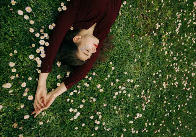 woman in maroon long sleeve shirt lying on white flower field
