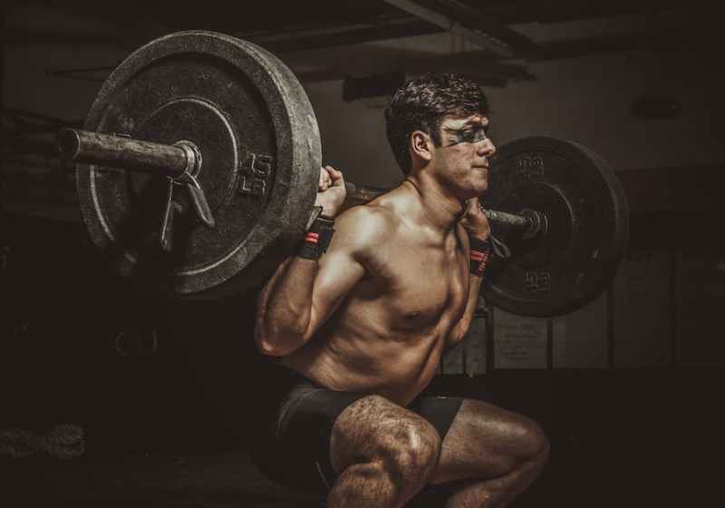 a topless man in black shorts doing squats with a barbell