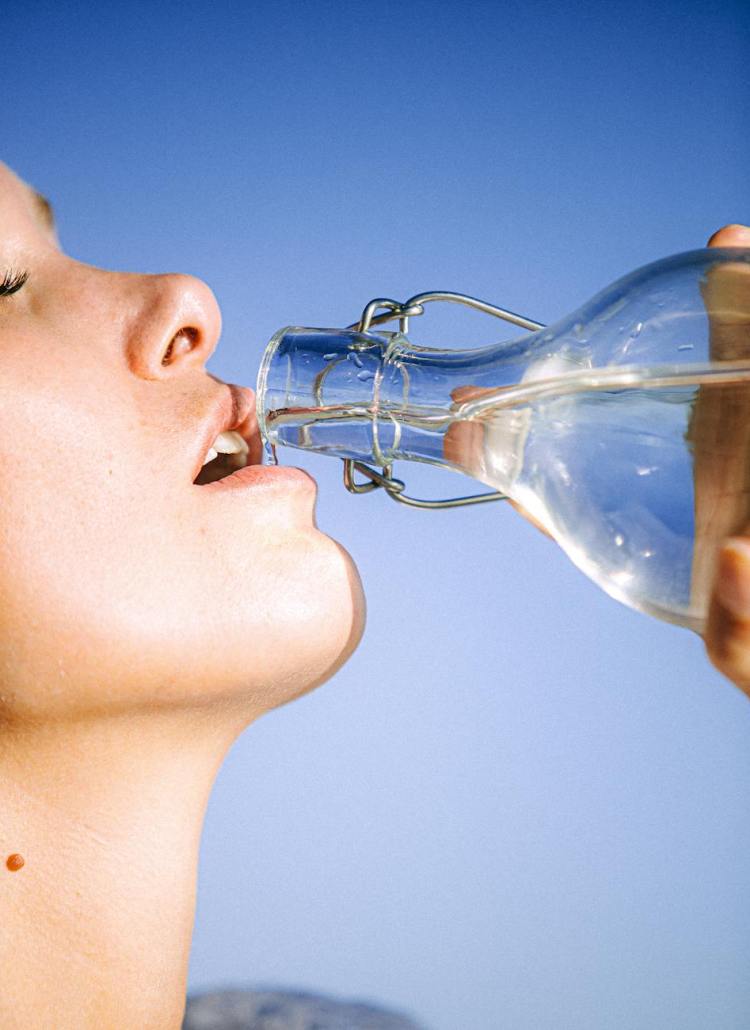 woman drinking water from glass bottle