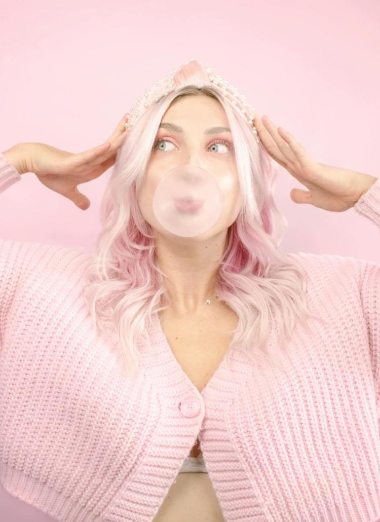 woman in pink cardigan blowing bubble gum