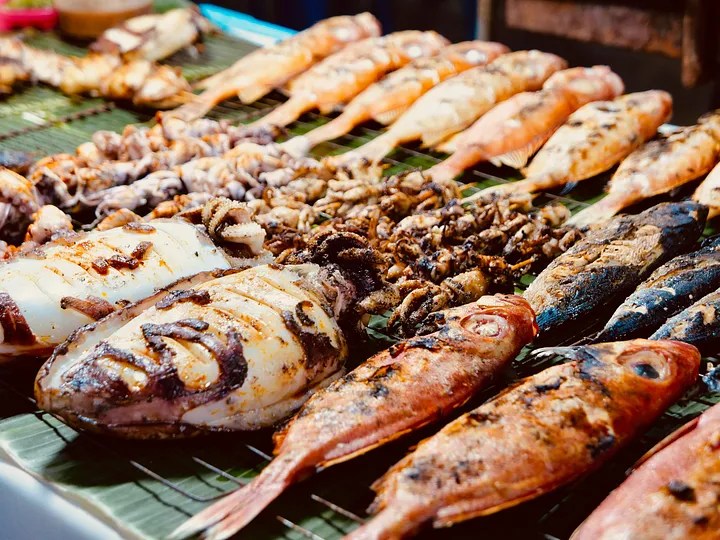 Grilled seafood including whole fish, squid, and octopus displayed on a banana leaf at a night market in Southeast Asia.