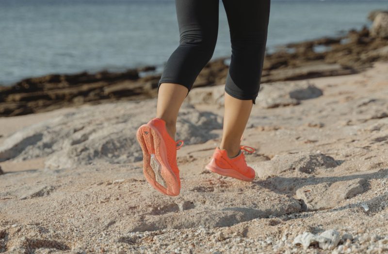 woman in black leggings and orange sneakers standing on brown sand near body of water during