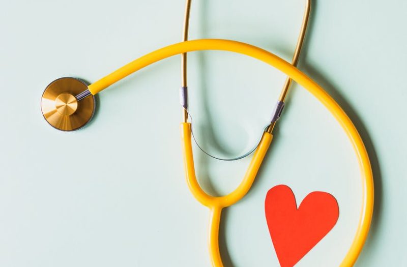 medical stethoscope with red paper heart on white surface