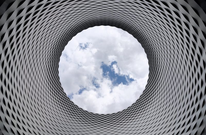 low angle photography of grey and black tunnel overlooking white cloudy and blue sky