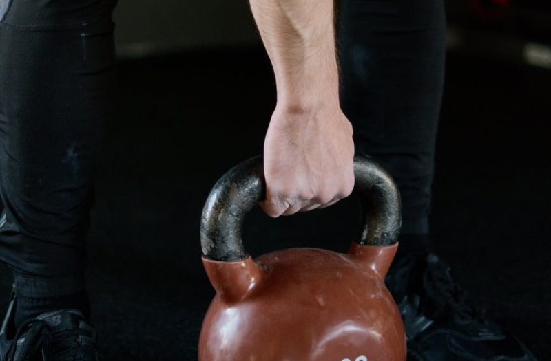 person in black pants holding red kettlebell