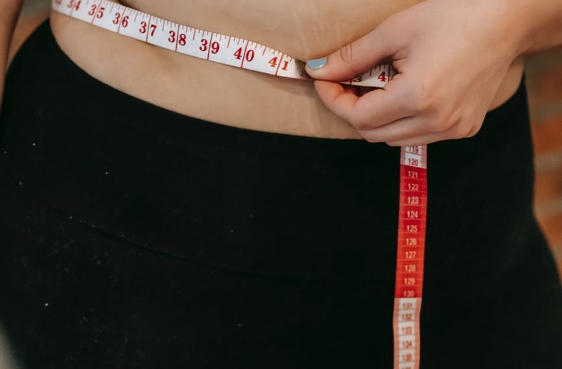 plus size woman using measuring tape on belly